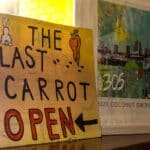 A yellow sign that reads “The Last Carrot, Open” Sitting on a shelf.