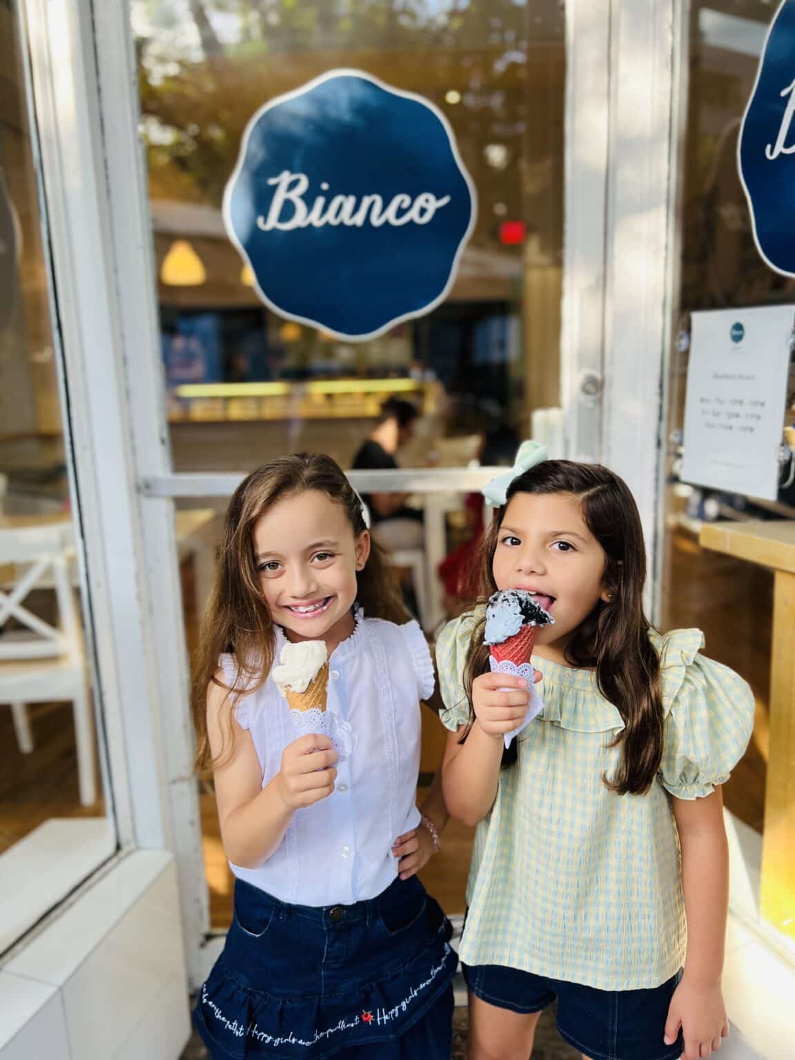 Two little girls standing next to each other eating ice cream in front of Bianco Gelato.