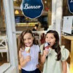 Two little girls standing next to each other eating ice cream in front of Bianco Gelato.
