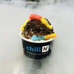 Gummy Worms sitting on top of crushed Oreo cookies, on top of ice cream in a black cup.