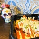 A mexican dish in a container next to a Day of the Dead skull vase.