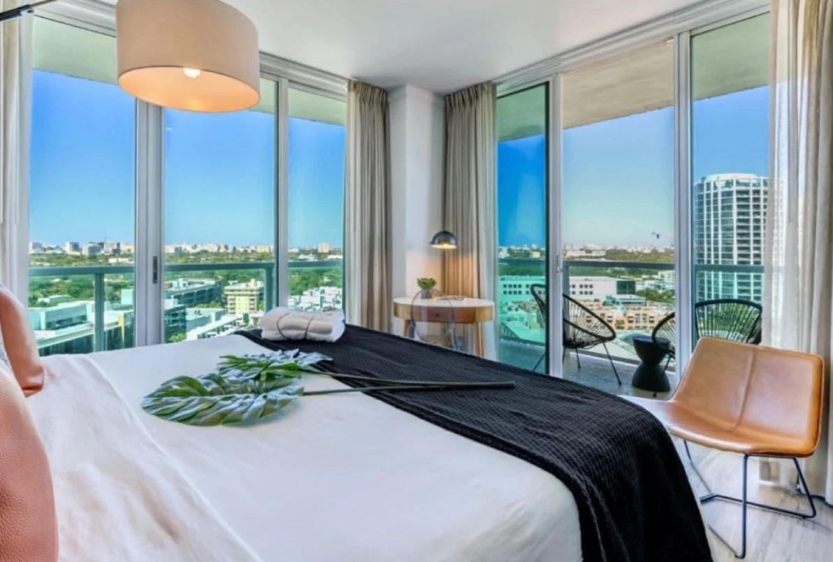Inside of a luxury hotel room with monstera leaves on the bed with a view overlooking the city.