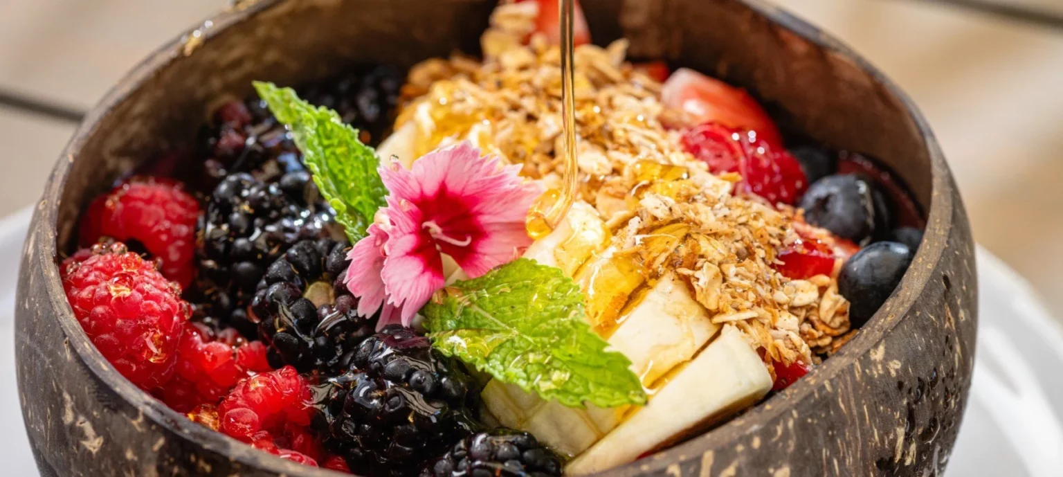 Acai bowl with fruit toppings, oats, honey and a flower.