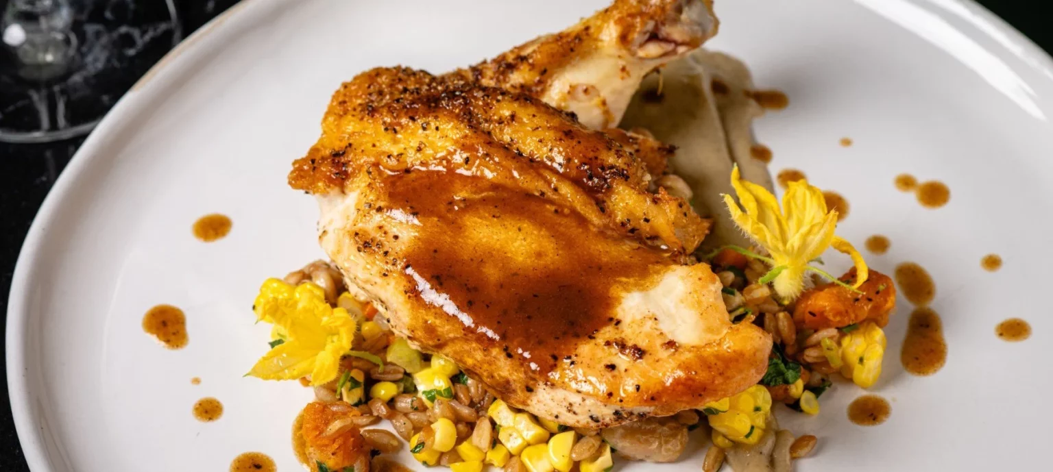 Roasted chicken plated on a dish garnished with gravy and corn.
