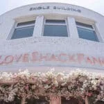 The outdoor sign of LoveShackFancy in Coconut Grove, FL. with pink flowers cascading below it.