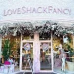 The exterior of the front window of LoveShackFancy with flowers all around it.