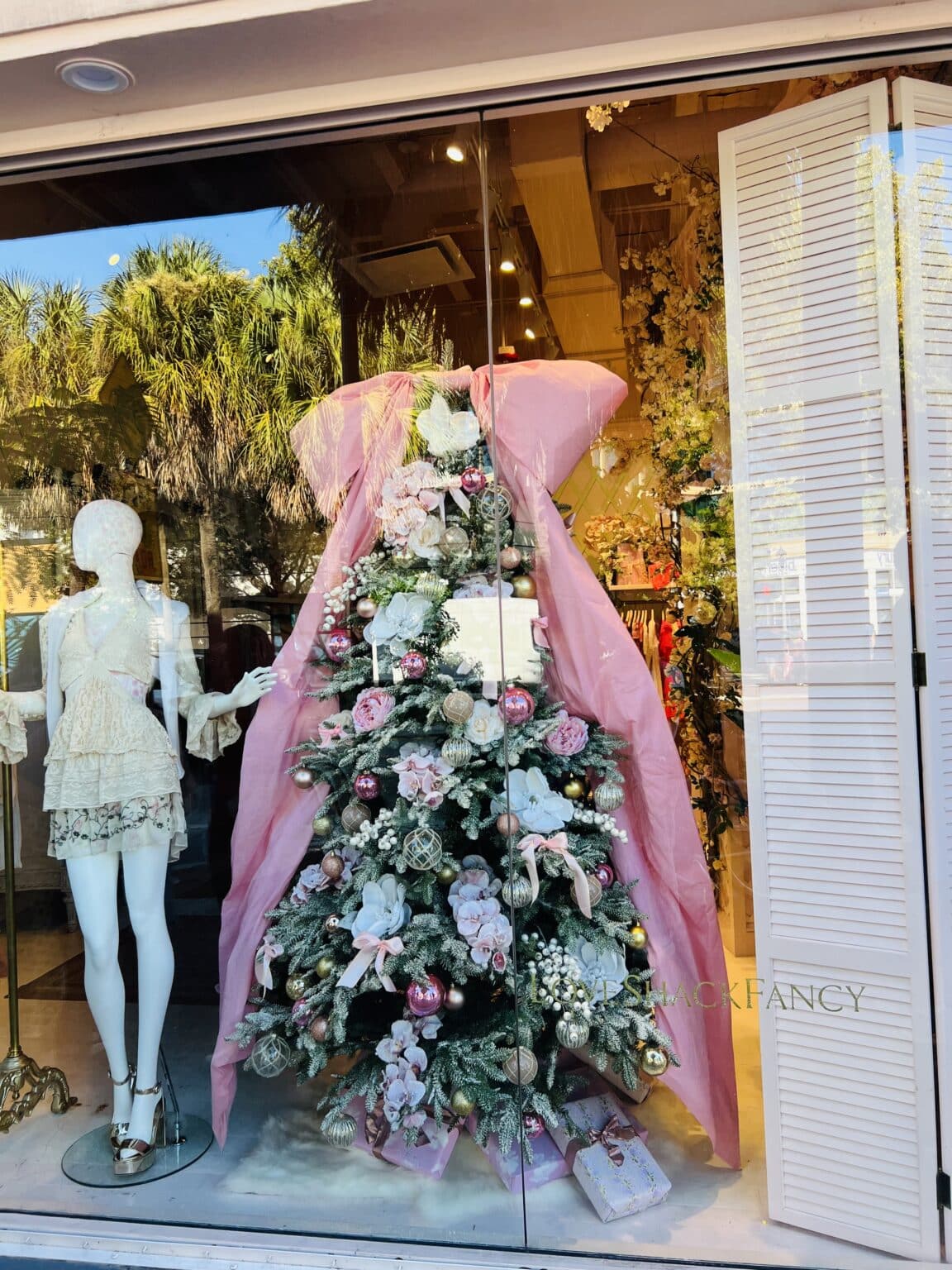 A Christmas tree window display next to a clothed mannequin.