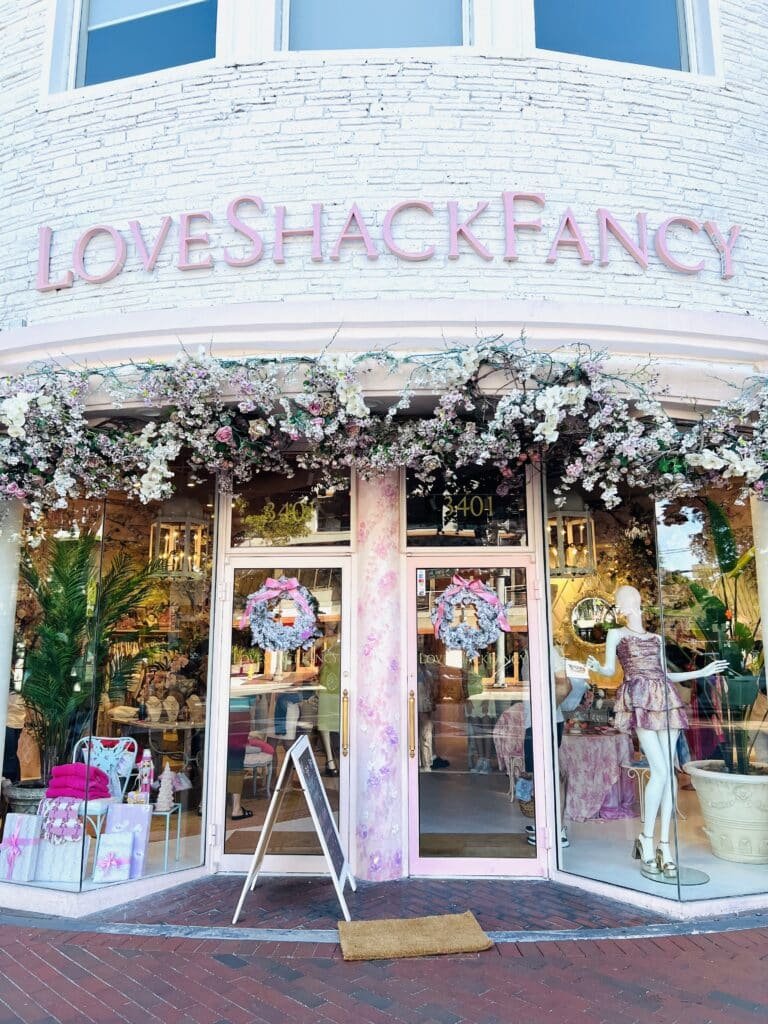 The exterior of the front window of LoveShackFancy with flowers all around it.