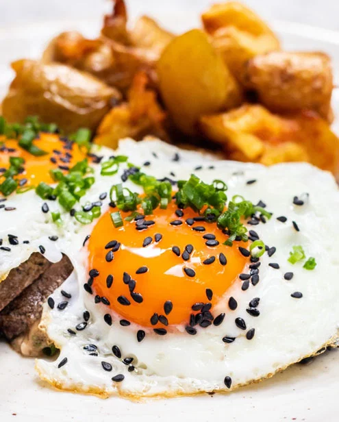 Friend egg topped with black sesame seeds, and chives, next to roasted potatoes.