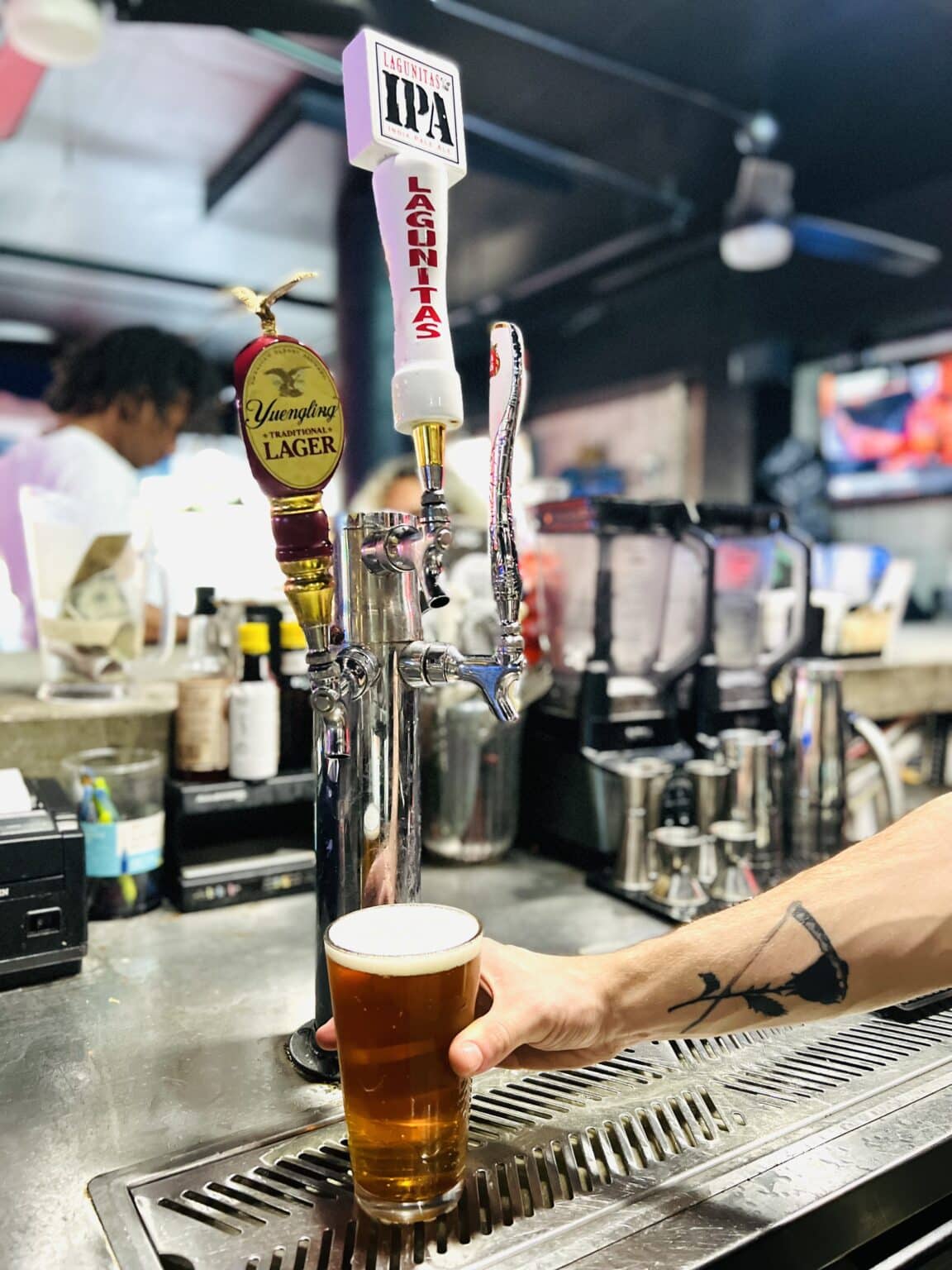 A person holding a glass of beer on a bar.