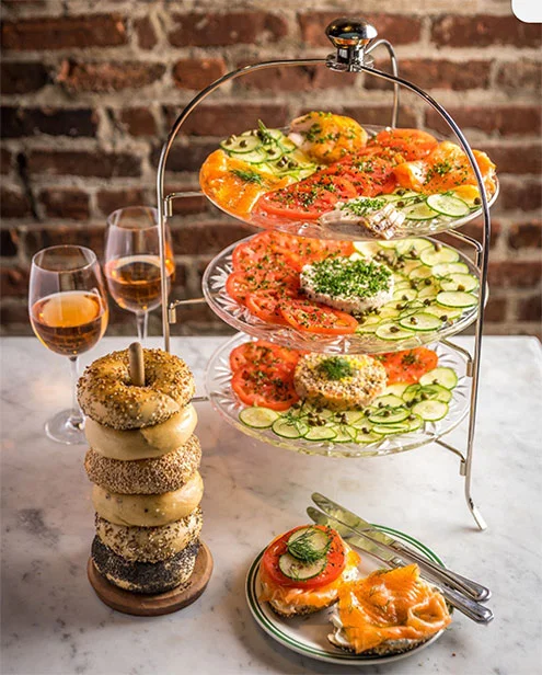 a tower of bagels next to a three tier platter of toppings.