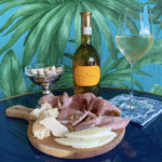 A bottle of wine next to a charcuterie board in front of a tropical wallpaper.
