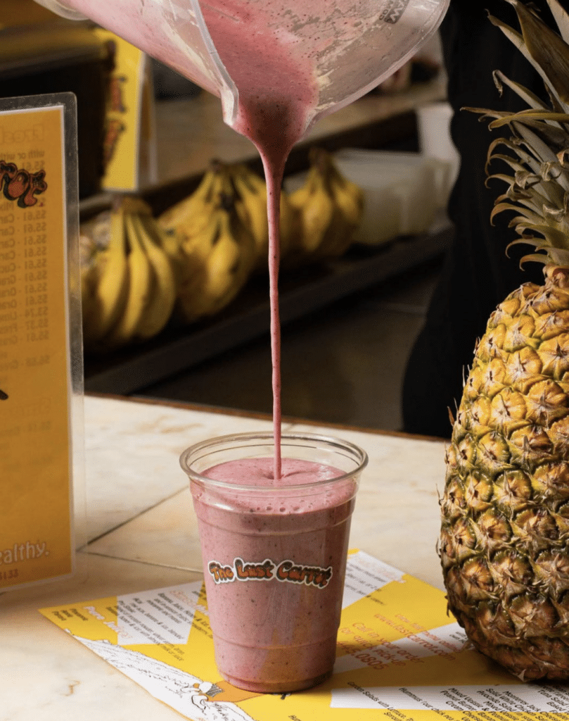A smoothie being poured into a cup from the The Last Carrot next to a pineapple.