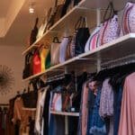 Interior of Allie and Chica boutique in Coconut Grove, FL. Showcasing racks of clothing items and shelves of purses on the wall.
