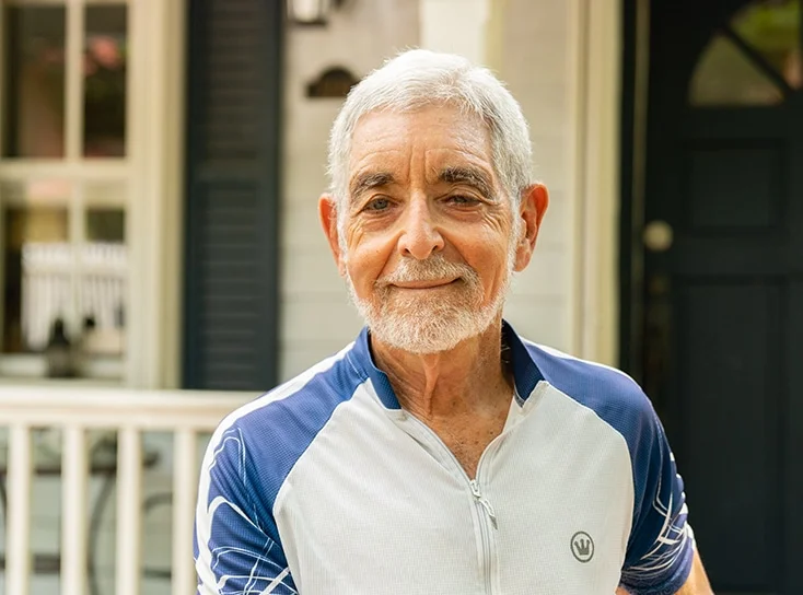 An elderly man with a beard smiling wearing a blue and white shirt.