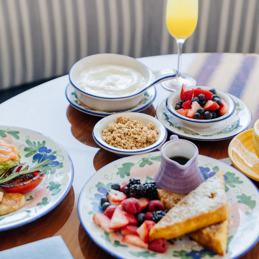 a variety of breakfast dishes, like berries and French toast, yogurt, granola, plated on floral plates