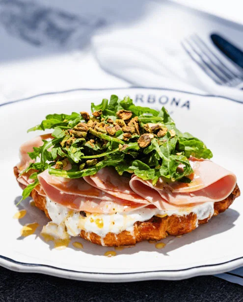 A brunch waffle topped with meat, arugula and nuts