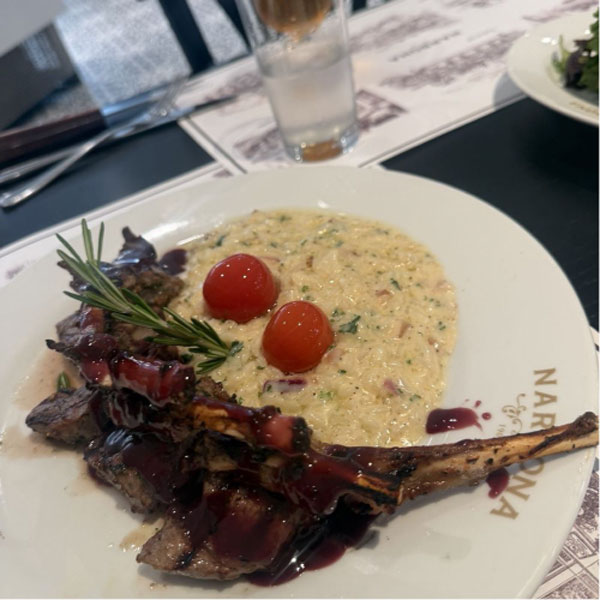 a plated lamb dish topped with a spruce of rosemary and tomatoes.