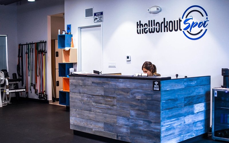The Workout Spot receptionist desk inside of the gym, with a person sitting in a chair, and the Logo on the wall.