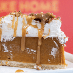 A piece of pumpkin pie on a plate topped with whipped cream and Carmel.