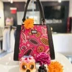 A brightly colored purse next to a skull decoration and flowers.