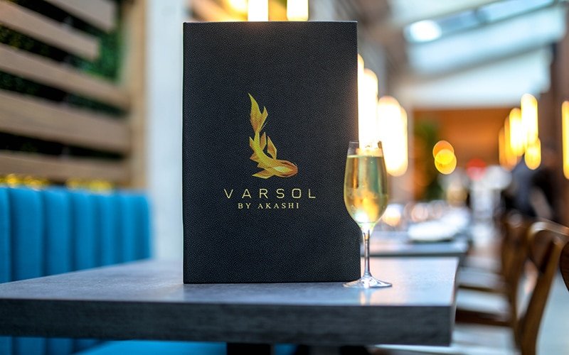 Varsol by Akashi menu sitting on a table next to a glass of white wine.