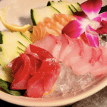 A plate of sliced fish with cucumber slices and flowers.