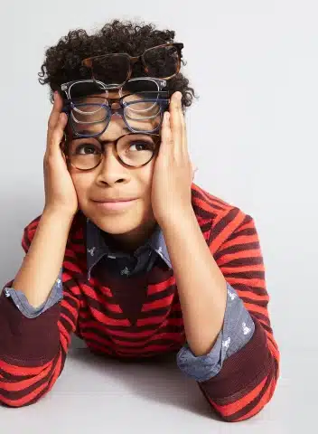A boy with two pairs of glasses on his face. He is wearing a red stripped shirt.