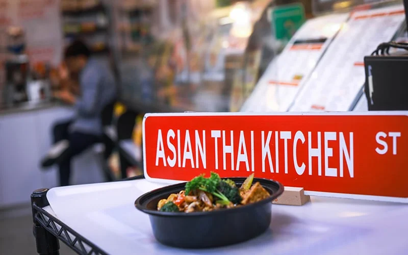 Red sign for the Asian Thai Kitchen Restaurant in Coconut Grove, FL. next to a bowl of food.