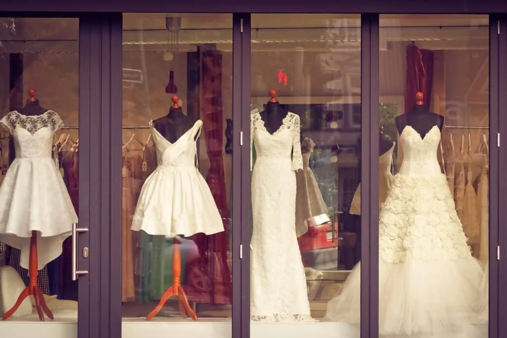 Bridal dresses, white in a front window display of a store.