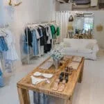 The inside of Market Boutique in Coconut Grove, FL. There are clothings hanging on the racks and a loveseat for sitting in the area.