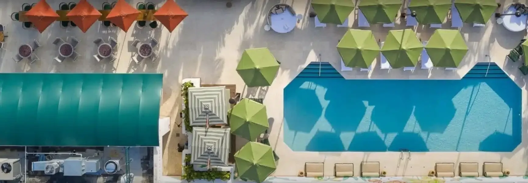 A bird's eye view of a pool and beach umbrellas in bright green and orange colors.