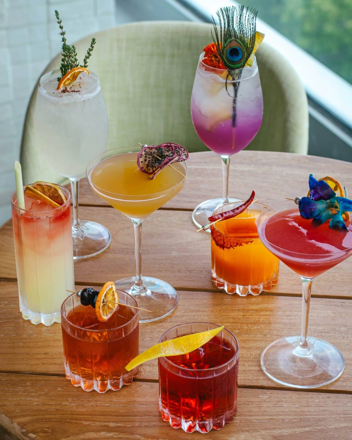 Fancy and unique drinks from Level 6 sitting on a wooden table. Drinks have been garnished with different items such as flowers, peacock feathers and orange slices.