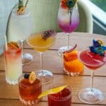 Fancy and unique drinks from Level 6 sitting on a wooden table. Drinks have been garnished with different items such as flowers, peacock feathers and orange slices.