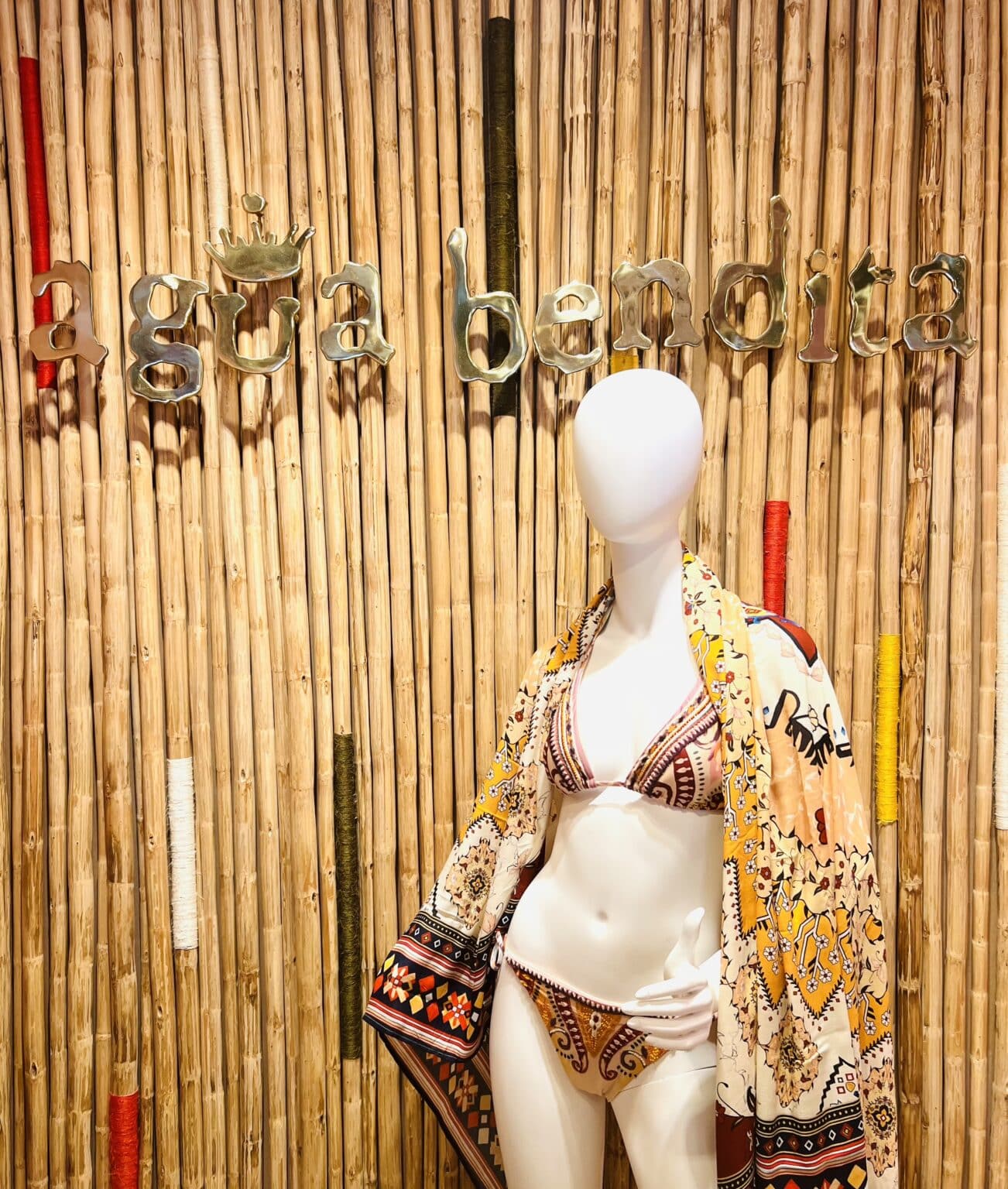 A mannequin with a bathing suit on standing in front of the store Agua Bendita sign.