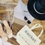 A market tote bag laid flat next to a tank top, sunglasses, shoes and a black hat.