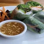 spring rolls on a plate next to peanut sauce and carrots.
