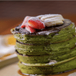 Green stack of pancakes from Minty Z, decorated with chocolate topping and fresh sliced strawberries.