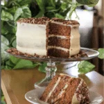 A fancy three layer cake with white icing. A piece of it is cut off and laying on a plate.