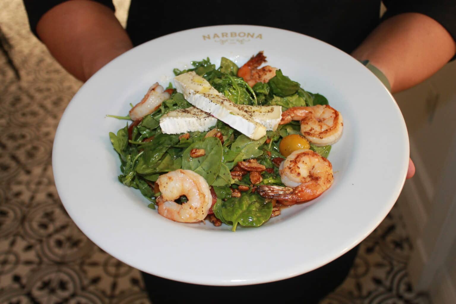 A spinach salad in a white bowl topped with shrimp, pecans and cheese.