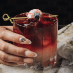A halloween themed drink being held by a hand with halloween themed nails.
