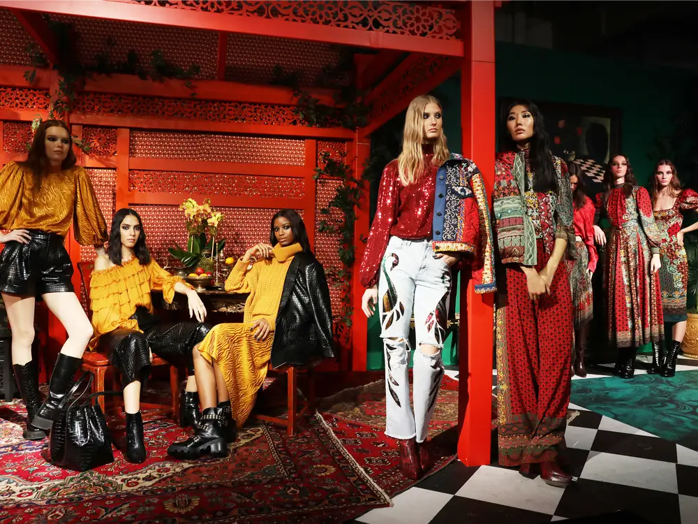 Models wearing outfits from the store Alice + Olivia, standing next to a red pergola.
