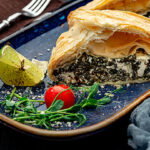 A flakey spinach pastry cut in half on a blue plate with garnishes.