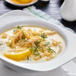 Greek Cuisine Avgolemono in a white bowl with a lemon slice and garnishes.