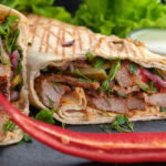 A gyro wrap cut in half and plated with red pepper slices.