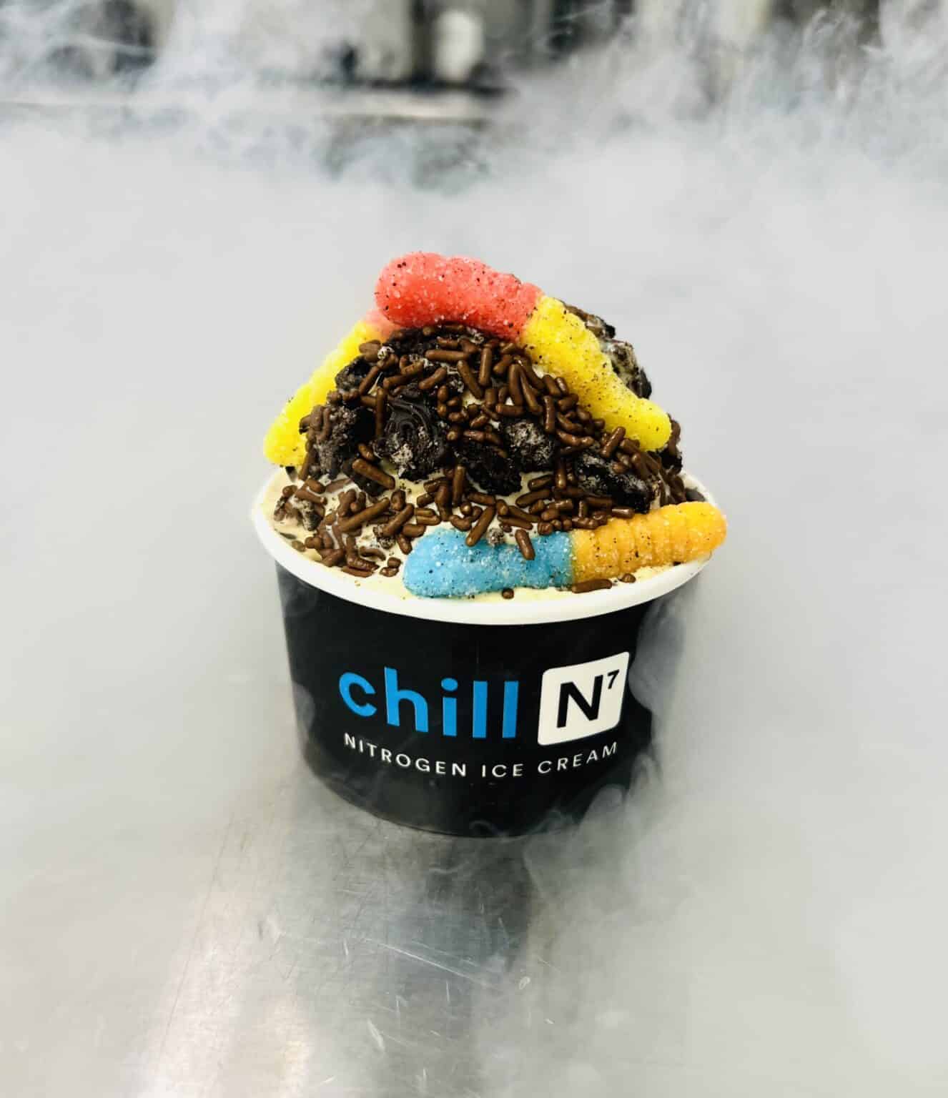 Gummy Worms sitting on top of crushed Oreo cookies, on top of ice cream in a black cup.