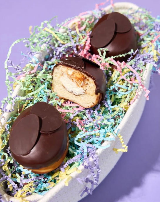 Donuts filled with creme and Dulce de leche and topped with chocolate sitting on top of a bowl filled with crinkle pastel paper
