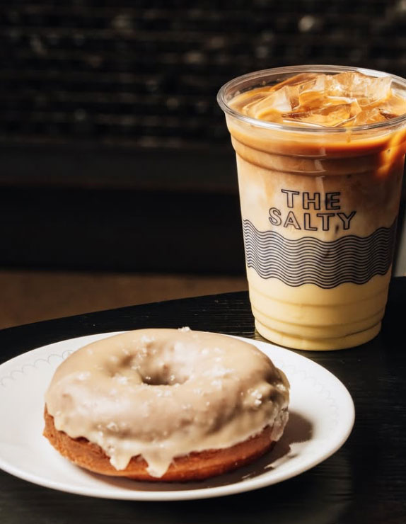 an iced latte served with a cake style donut topped with icing.