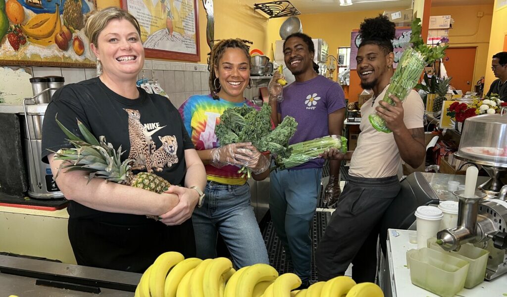 A group of people holding fruits and veggies in a smoothie bar.