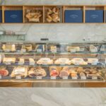 meats and cheeses displayed in a case with breads in baskets.